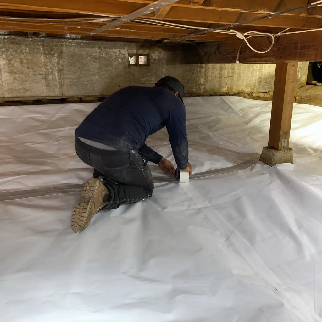 Technician installing white vapor barrier insulation in a crawl space